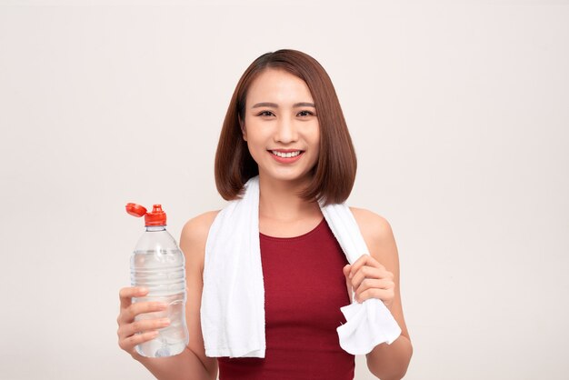 Chica deportiva con botella de agua y una toalla sobre los hombros en la luz