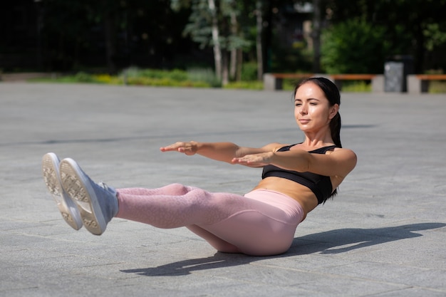 Chica deportiva bronceada delgada con ropa deportiva haciendo ejercicios de abdominales en el parque