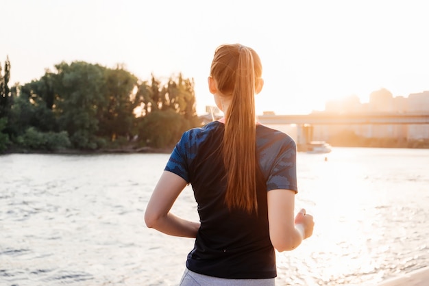 Chica deportiva en una carrera en una ciudad cerca de un río, en el fondo de un puente y un parque. Vista trasera