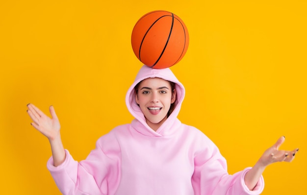 Chica deportiva divertida divirtiéndose con pelota de baloncesto sobre fondo amarillo