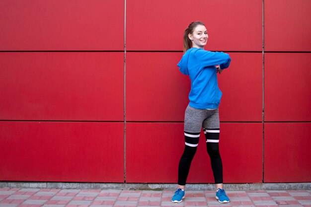 Foto chica deportiva está entrenando contra una pared roja en la calle