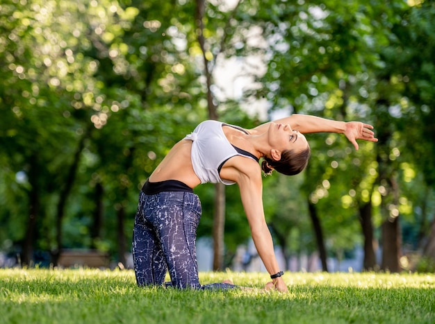 Chica deportiva haciendo yoga en la naturaleza y entrenando su equilibrio. Mujer joven haciendo ejercicio y estirando su cuerpo en verano