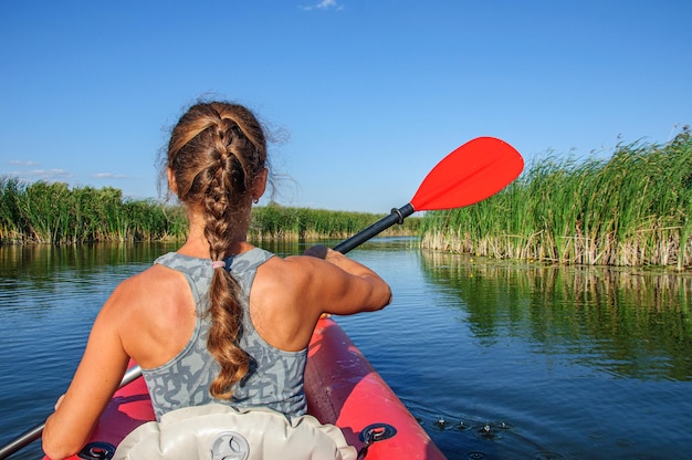 Una chica deportiva en un kayak rojo rema a lo largo del río Zdvizh. Ucrania