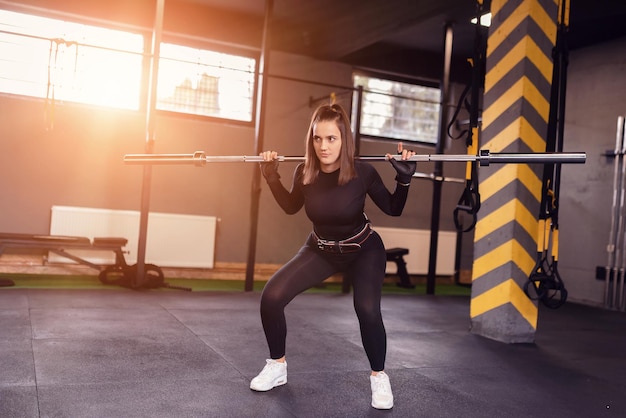 chica deportiva se pone en cuclillas con entrenamiento con barra.