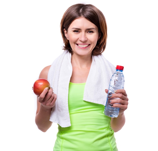 Foto chica deportiva sosteniendo una manzana y agua con una toalla en su cuello aislada sobre un fondo blanco