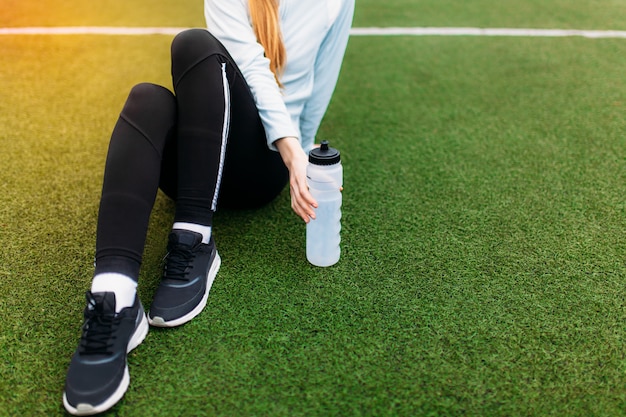 Foto chica descansando después de un buen entrenamiento. chica después del ejercicio, agua potable en el campo de fútbol. retrato de muchacha hermosa en ropa deportiva.