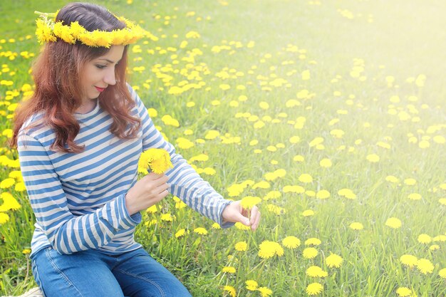 Chica descansando en un día soleado en una pradera de diente de león amarillo