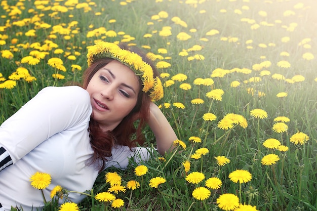 Chica descansando en un día soleado en una pradera de dientes de león amarillos