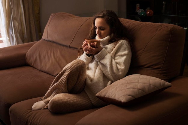 Chica descansando en el sofá oliendo una taza de caféxA