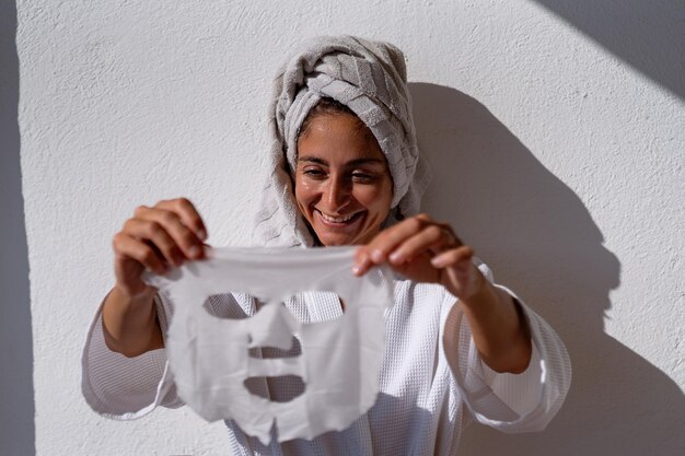 Foto una chica después de una ducha en una túnica blanca y una toalla con una máscara cosmética en su cara