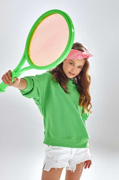 Chica con diadema rosa muestra raqueta de tenis en estudio