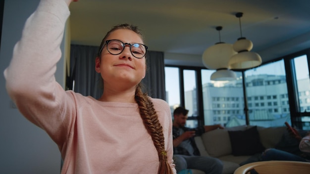 Chica diligente escolarización en casa Chica con gafas levantando la mano durante la lección en línea