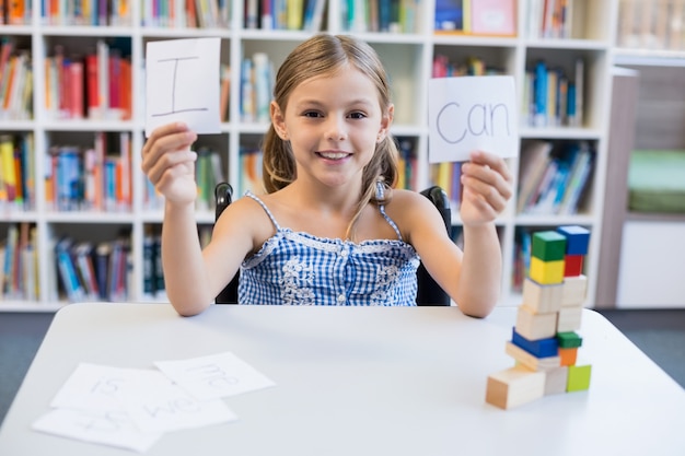 Chica discapacitada sosteniendo un cartel que dice I Can en la biblioteca