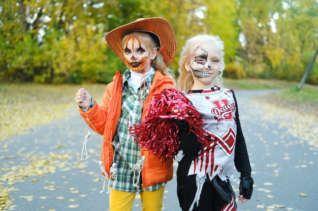 Una chica con un disfraz de animadora con maquillaje de esqueleto de media  cara y una chica con maquillaje de calabaza