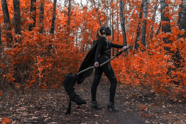 Una chica con un disfraz de bdsm y una máscara negra en un bosque rojo. Una idea para halloween.