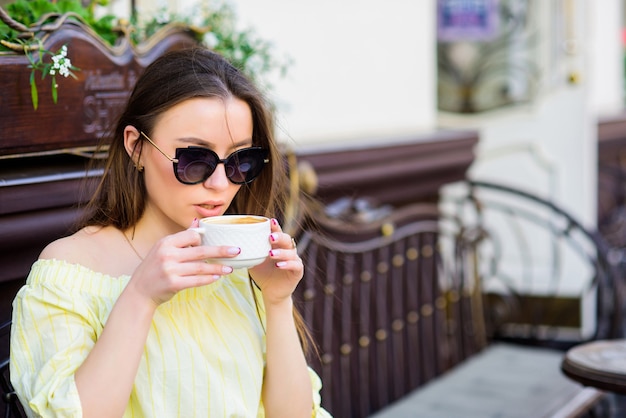 Chica disfruta del café de la mañana. Mujer con gafas de sol beber café al aire libre. Chica relajarse en la taza de café capuchino. Dosis de cafeína. Café para un día lleno de energía. Esperando fecha. Hora del desayuno en la cafetería.