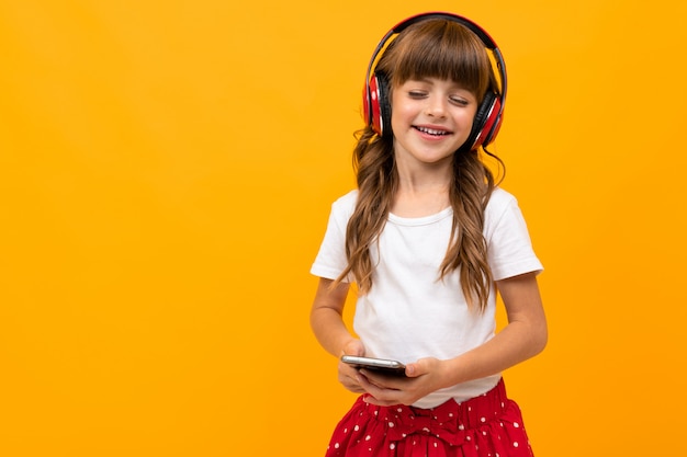 Chica disfruta escuchando música con auriculares y sosteniendo un teléfono en sus manos en amarillo