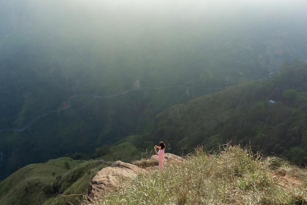 Chica disfruta de una vista a la montaña mientras está de pie en un acantilado