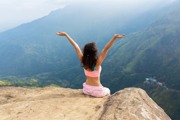 Chica disfruta de una vista a la montaña mientras está de pie en un acantilado