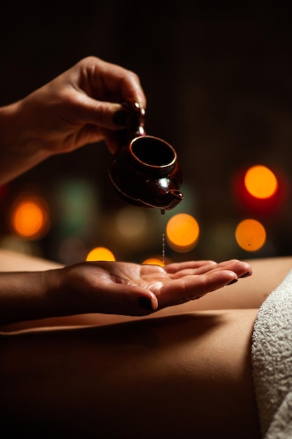 Chica disfrutando de un masaje terapéutico con aceite en el spa con iluminación oscura, cerrada