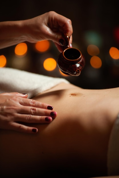 Chica disfrutando de un masaje terapéutico con aceite en el spa con iluminación oscura, cerrada