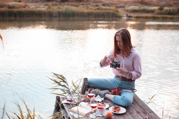 Chica disfrutando de un picnic en un muelle de madera en una orilla del río de verano brillante