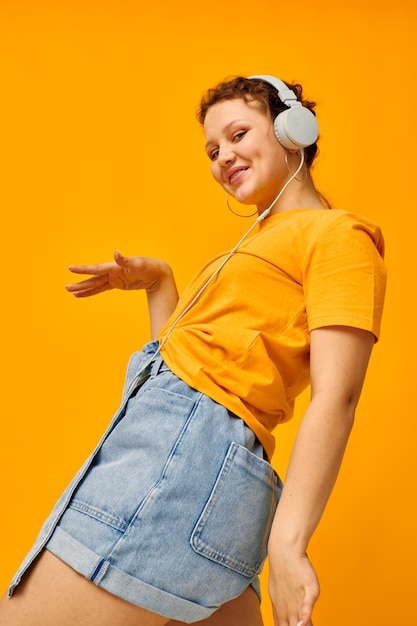 Chica divertida escuchando música en auriculares estilo juvenil fondo amarillo inalterado