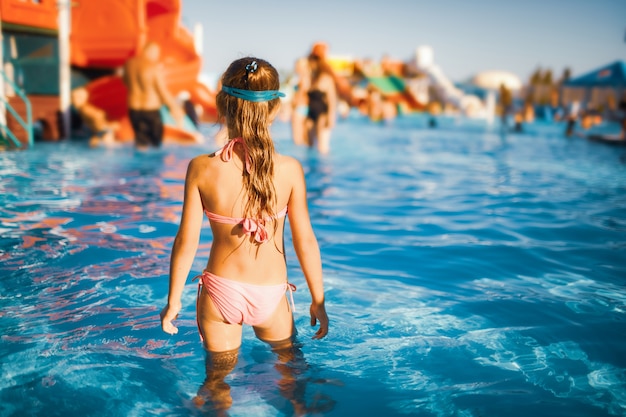 Chica divertida en gafas azules para nadar se encuentra en una piscina con agua clara y transparente disfrutando del cálido sol de verano