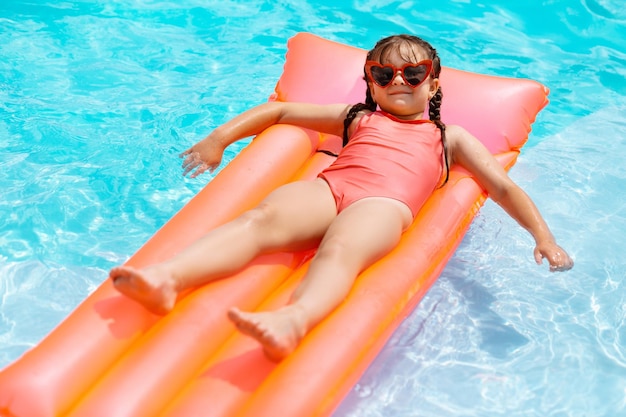 Una chica divertida con gafas de sol relajándose en un colchón de aire en la piscina