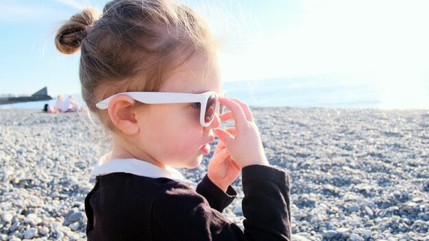 Chica divertida juega con gafas de sol en Pebble Beach al atardecer