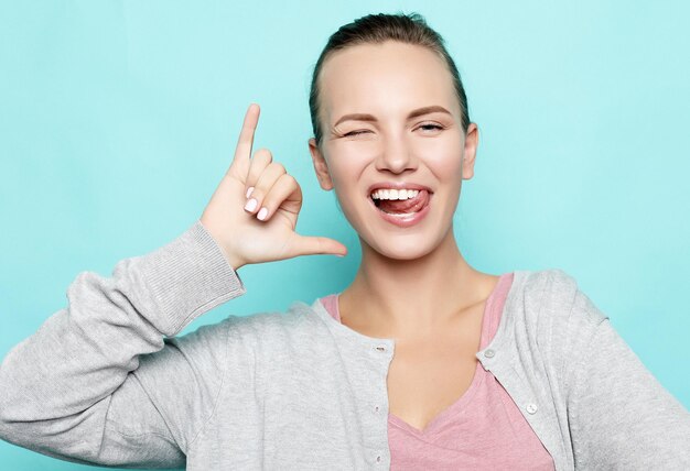 Chica divertida mostrando su lengua mientras posa contra el fondo del estudio Hembra joven positiva emocional haciendo muecas