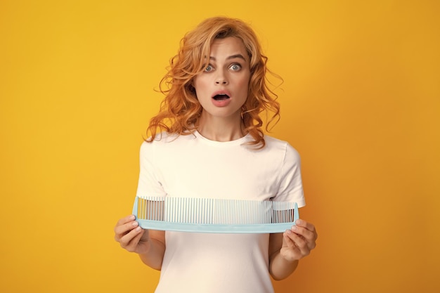 Chica divertida peinando el cabello mujer pelirroja con un peine aislado sobre fondo amarillo