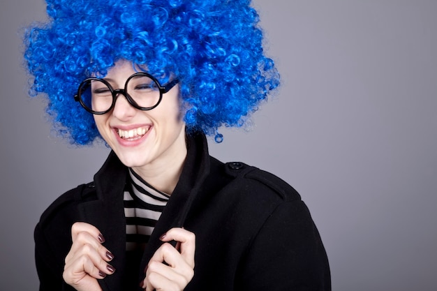 Chica divertida de pelo azul con gafas y abrigo negro.