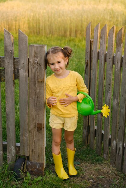 Una chica divertida con una regadera de plástico se encuentra en la puerta de una antigua valla que conduce al jardín