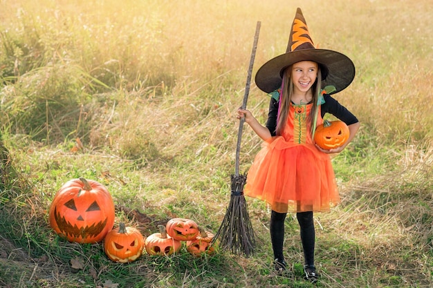 Chica divertida con un sombrero grande y un vestido de bruja naranja.