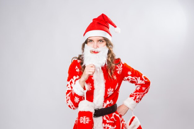 Chica divertida vistiendo traje de santa de Navidad y barba sobre blanco