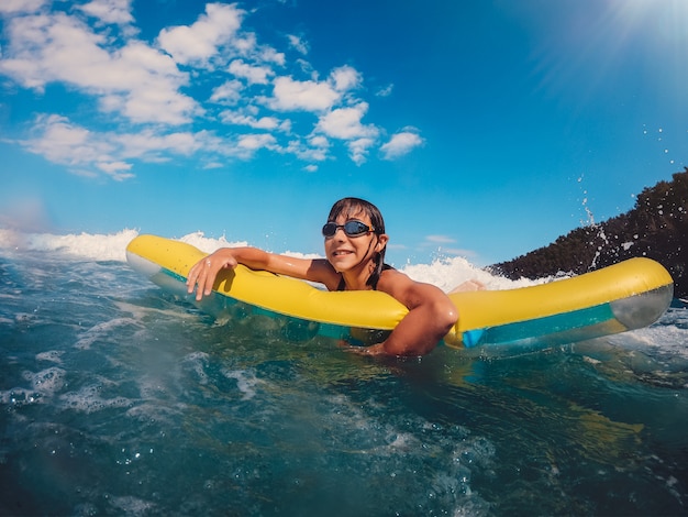 Chica divirtiéndose flotando en la cama de aire en el mar