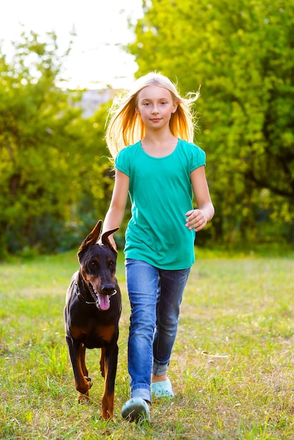 Chica con dobermann en el parque de verano.