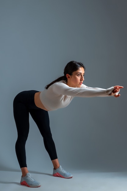 Foto chica doblando el cuerpo hacia adelante con los brazos extendidos sobre la pared gris