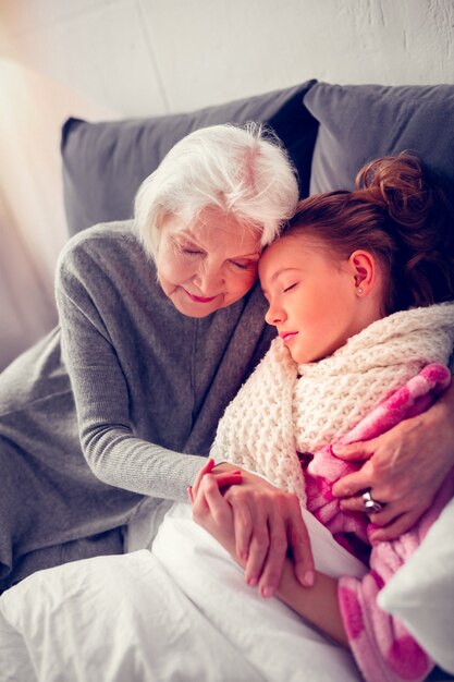 Chica dormida. Niña enferma de cabello oscuro que se queda dormido cerca de su abuela cariñosa y cariñosa mientras se siente enferma