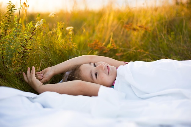 La chica duerme en la cama en la hierba, Sweet se estira y bosteza con sueño, buenos días al aire libre. Respetuoso con el medio ambiente, sueño saludable, Protección contra mosquitos, naturaleza limpia, ecología, salud infantil