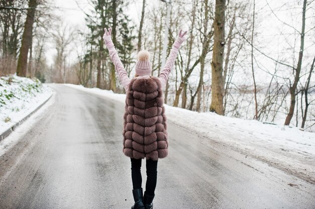 Chica elegante en abrigo de piel y sombreros en día de invierno en la carretera.