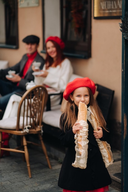 Una chica elegante con baguettes se para cerca de la tienda en el contexto de sus padres