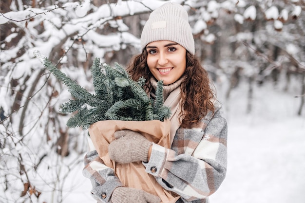 Una chica elegante en un bosque nevado sostiene una bolsa de kraft de una rama de abeto nobilis