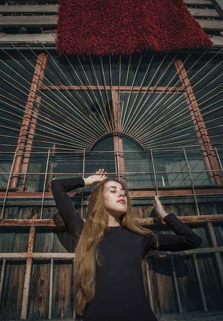 Chica elegante con cabello largo y hermoso con un vestido negro contra una pared marrón como una madonna moderna.