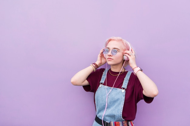 Chica elegante con cabello rosado y gafas de sol trae música a los auriculares