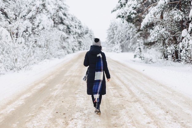 Chica elegante caminando en medio de una carretera en un bosque nevado