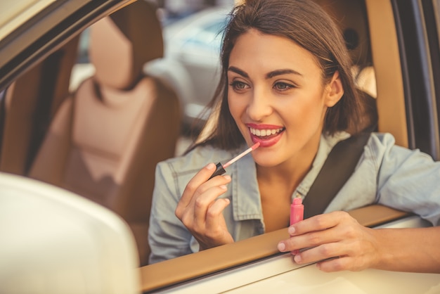 Chica elegante está usando un brillo de labios y sonriendo mientras conduce.