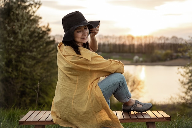 Chica elegante en estilo casual descansa cerca del lago al atardecer por la noche