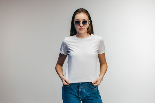 Chica elegante con gafas con camiseta blanca posando en el estudio